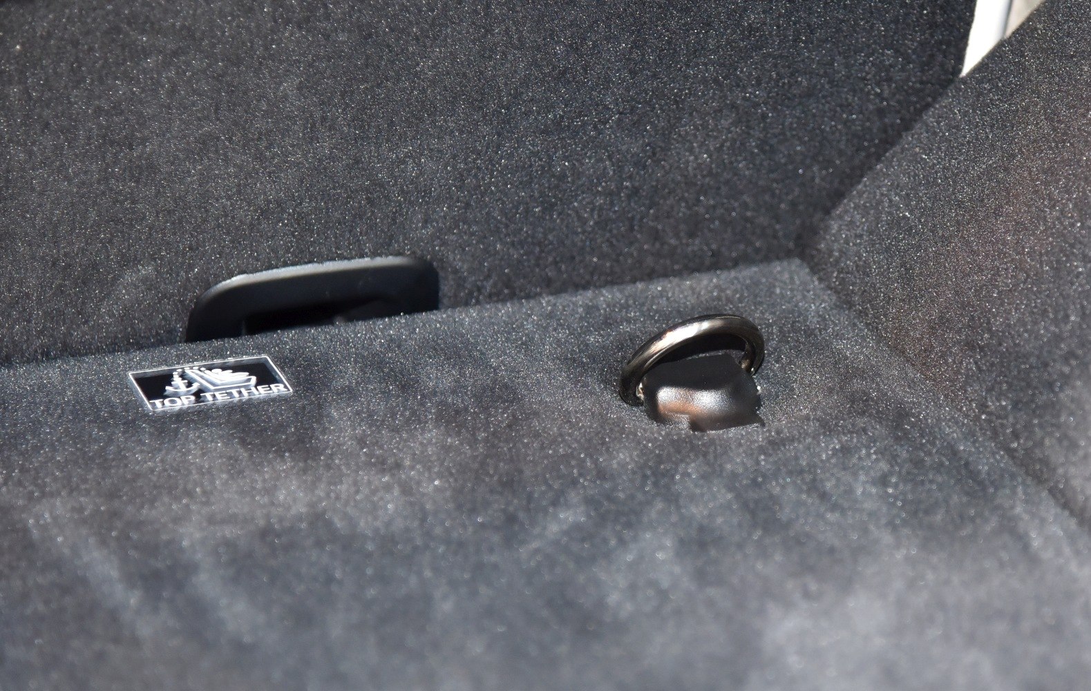 Close-up of a top tether child seat anchor in dark carpeted rear compartment