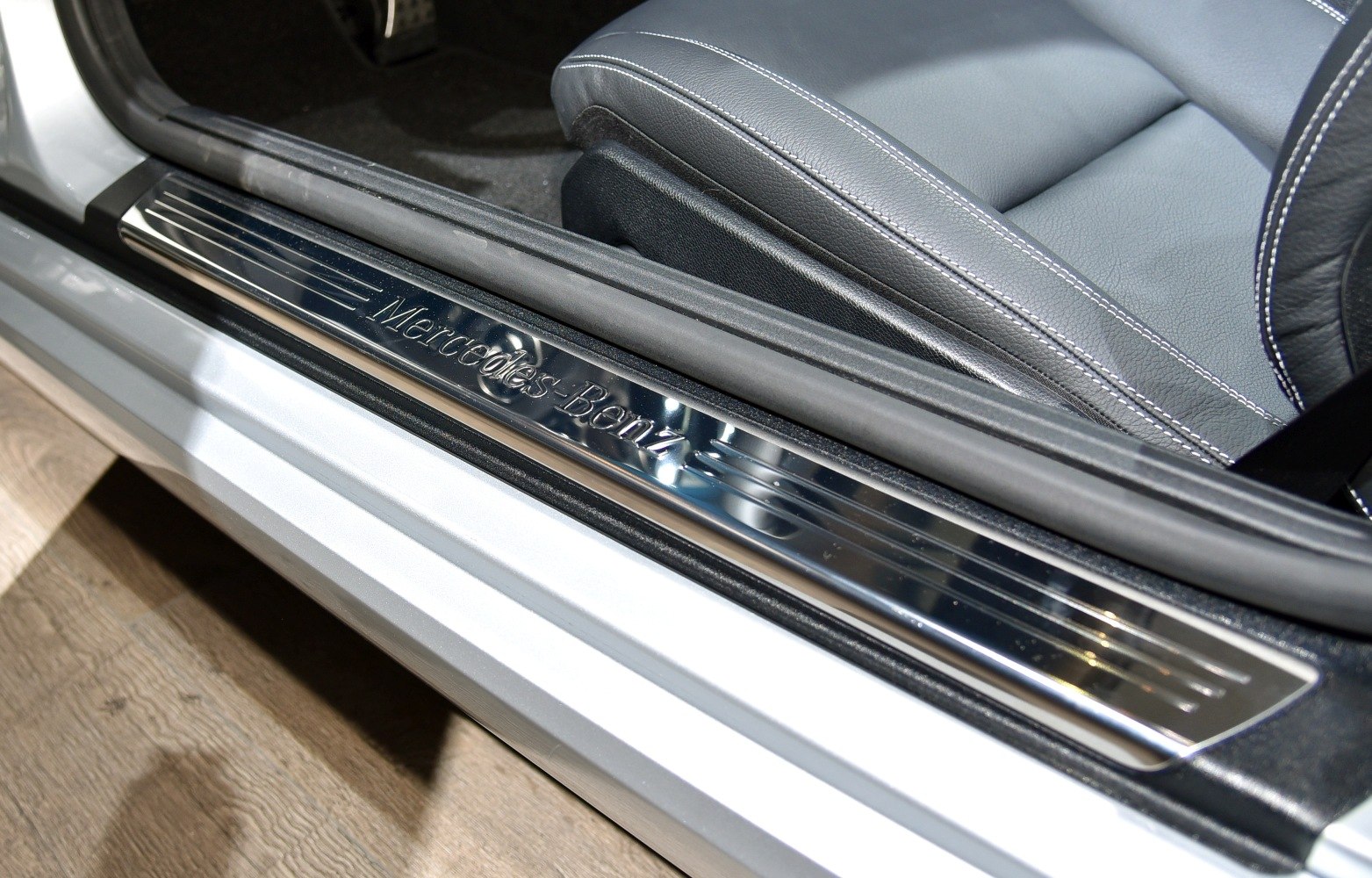 Polished metal door sill plate with Mercedes-Benz logo and leather car seat stitching