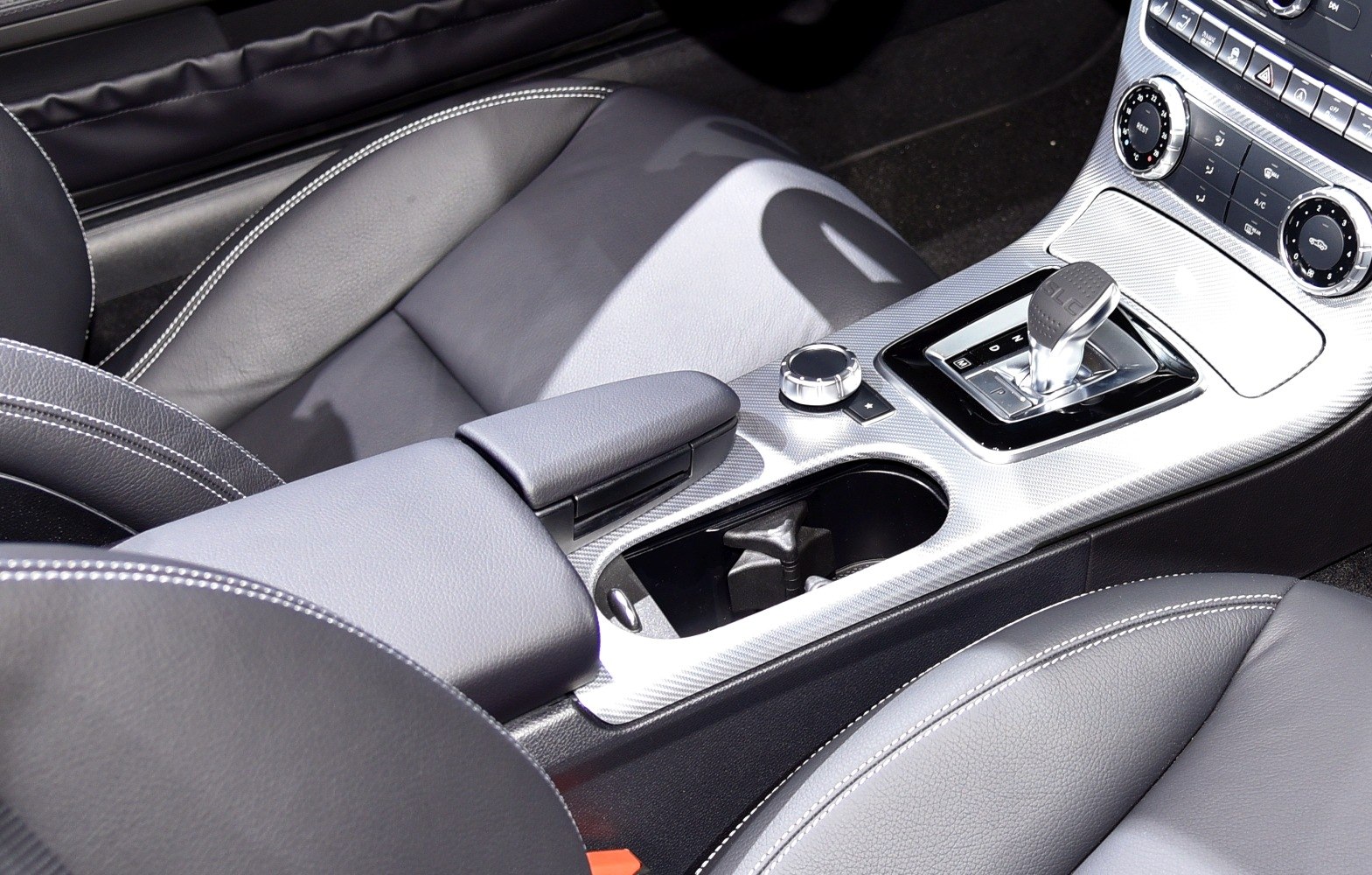 Center console with gear shifter, control dial, and leather seats with white stitching