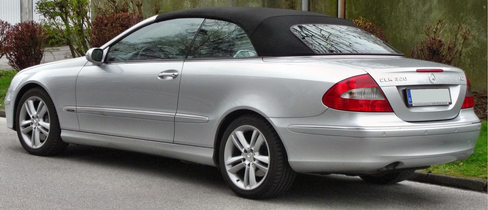 Silver convertible with black soft top and alloy wheels seen from rear side