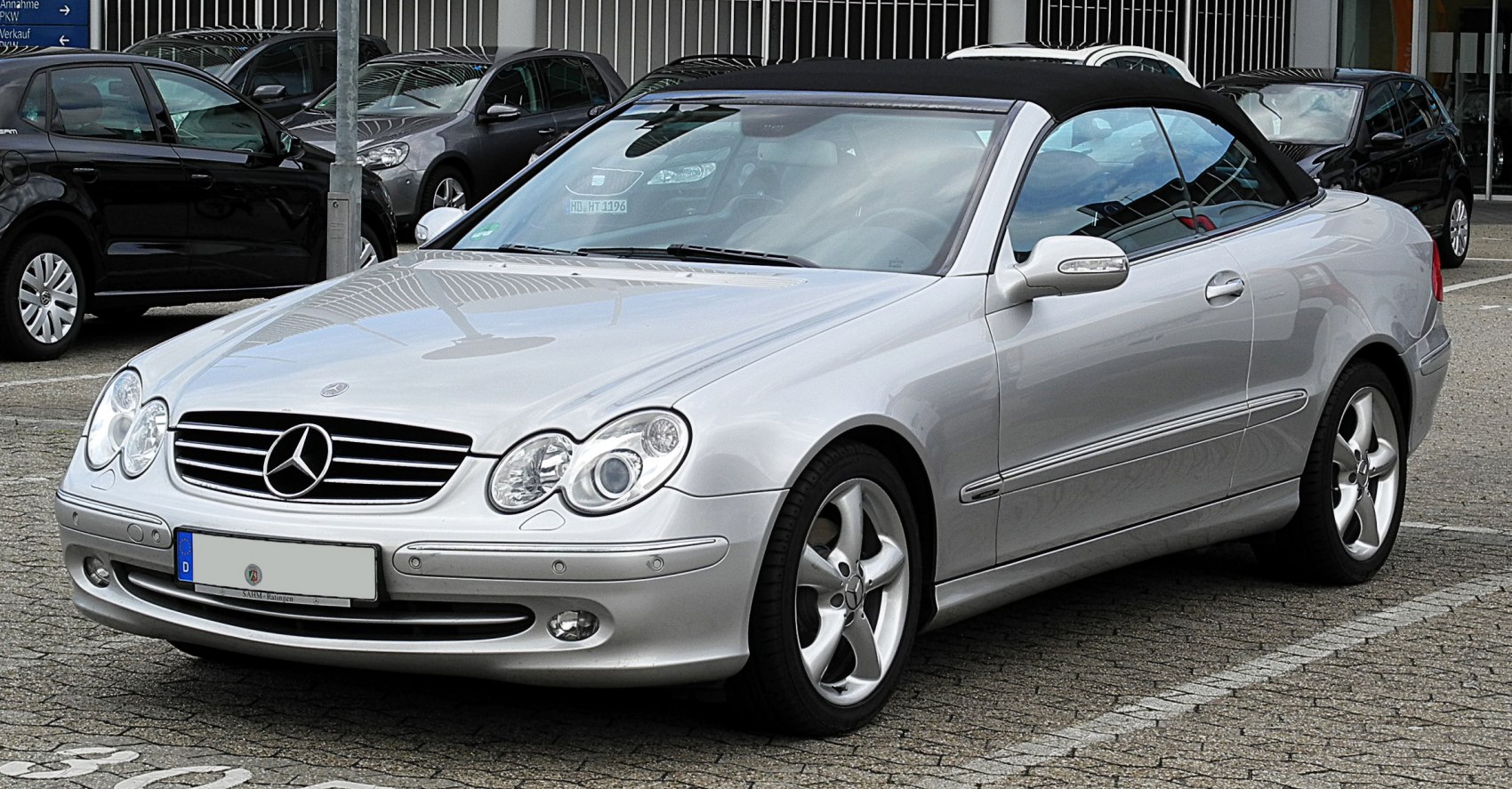 Silver convertible with black soft top parked front side view