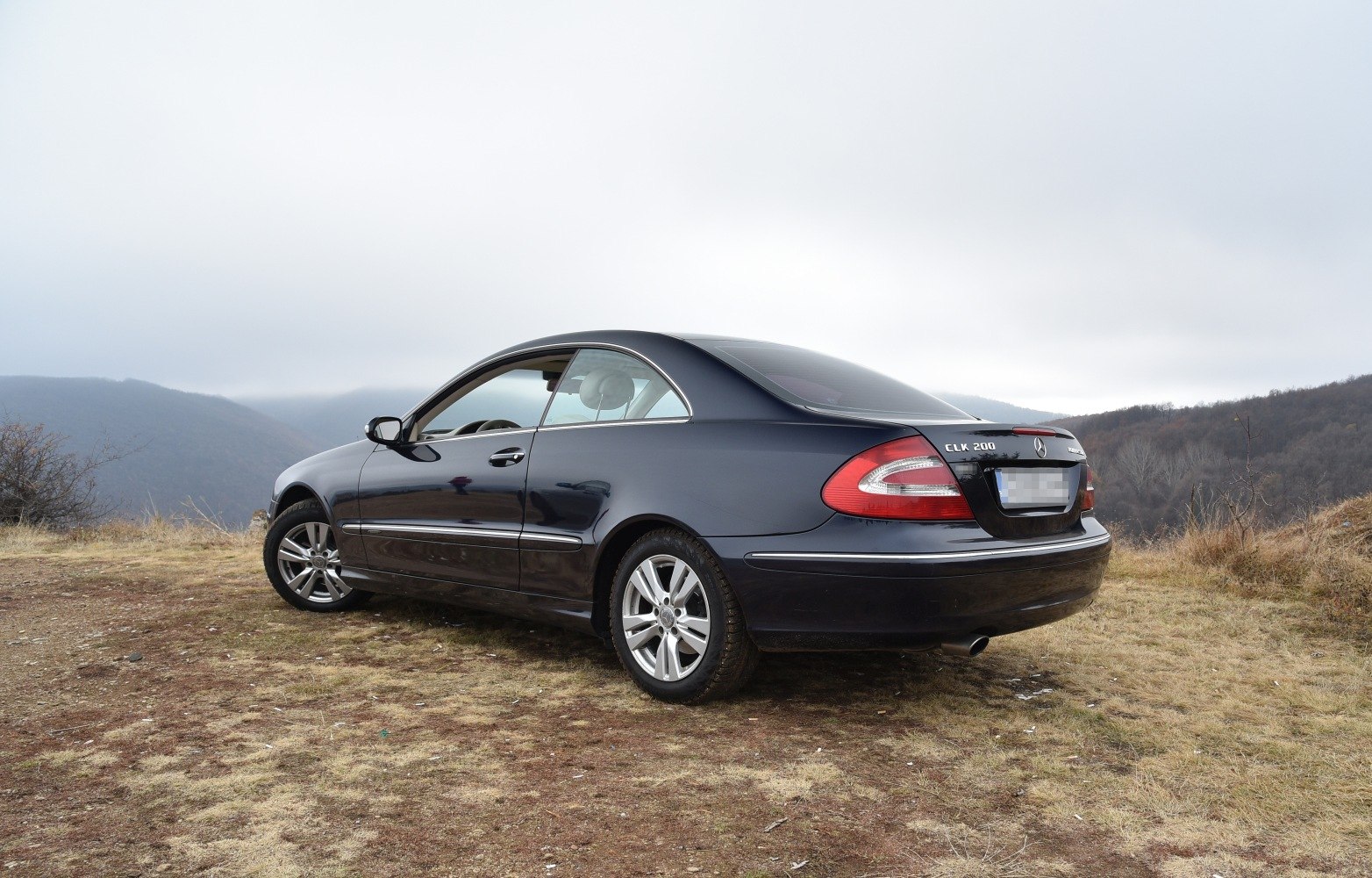 Rear-side view of a luxury 2-door coupe with alloy wheels on rough terrain.