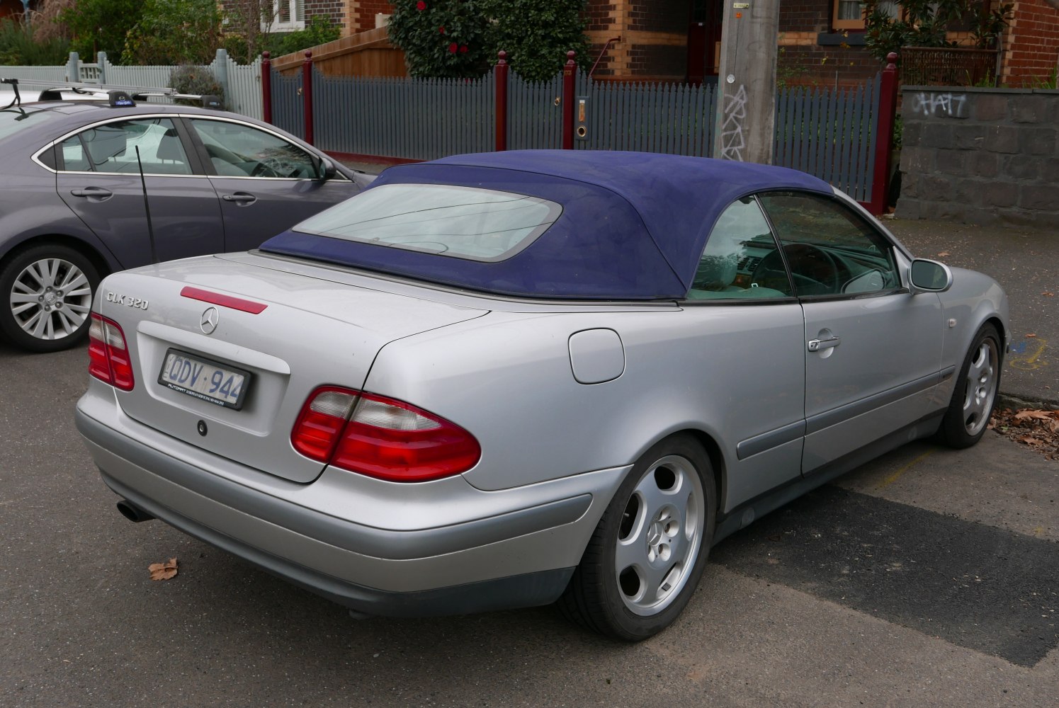 Silver convertible with blue soft top and alloy wheels from rear-side view