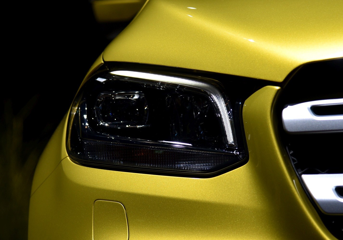 Close-up of LED headlight and front grille on metallic yellow vehicle