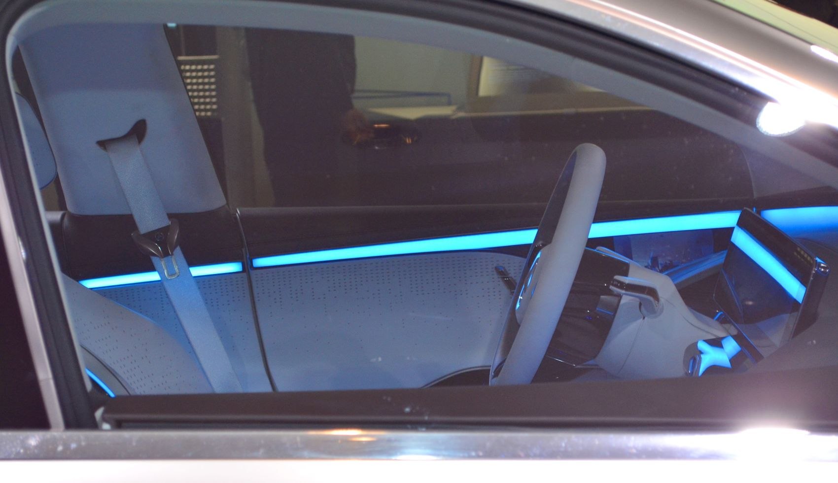 Illuminated blue ambient lighting and modern steering wheel inside a futuristic vehicle.