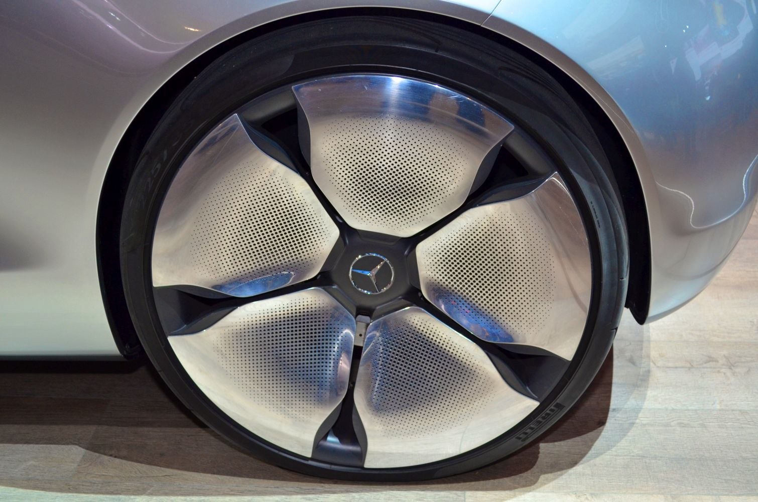 Close-up of a futuristic perforated alloy wheel with five uniquely curved spokes.