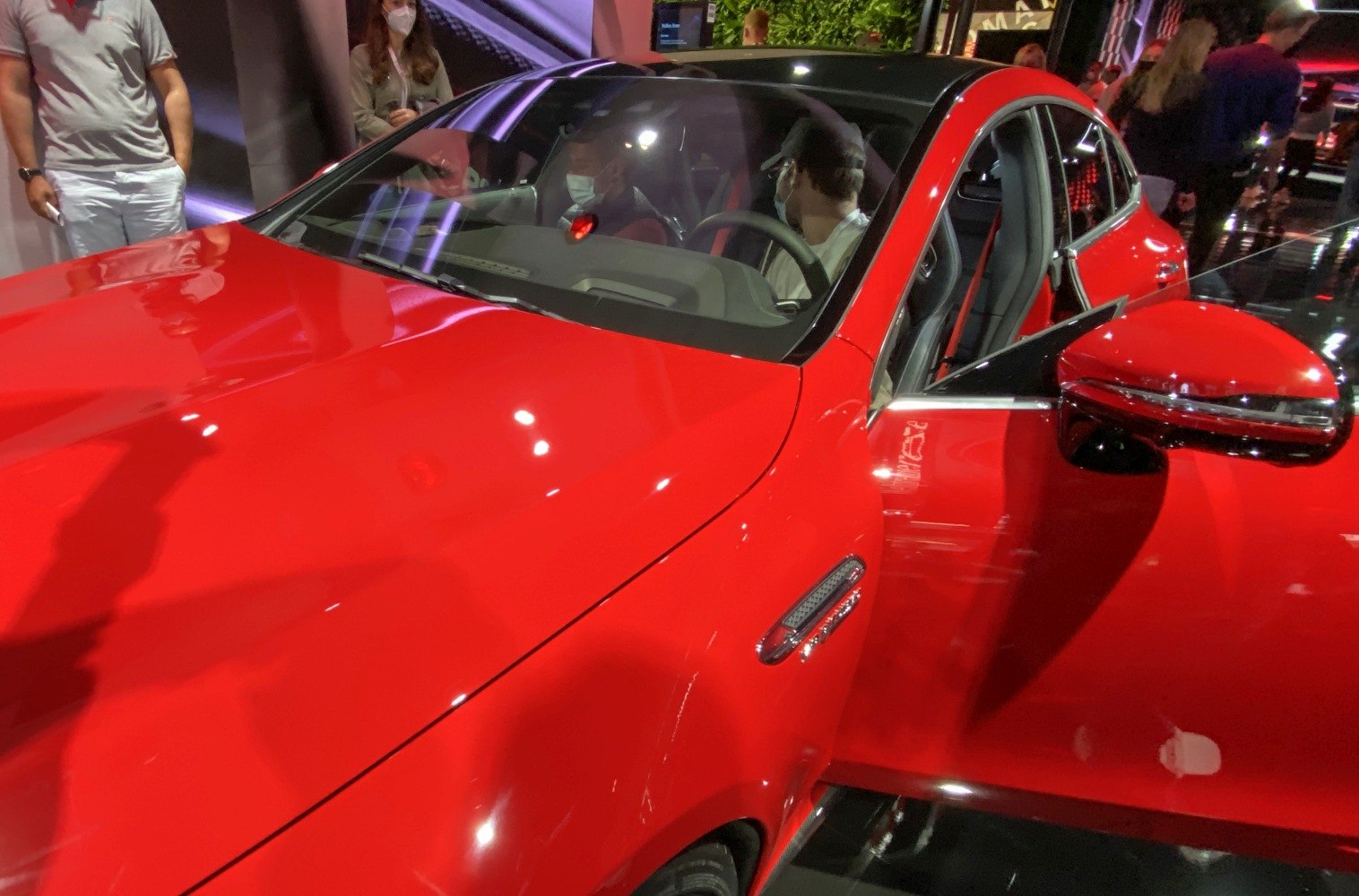 Glossy red front hood, side mirror, and open driver door of a luxury sports vehicle