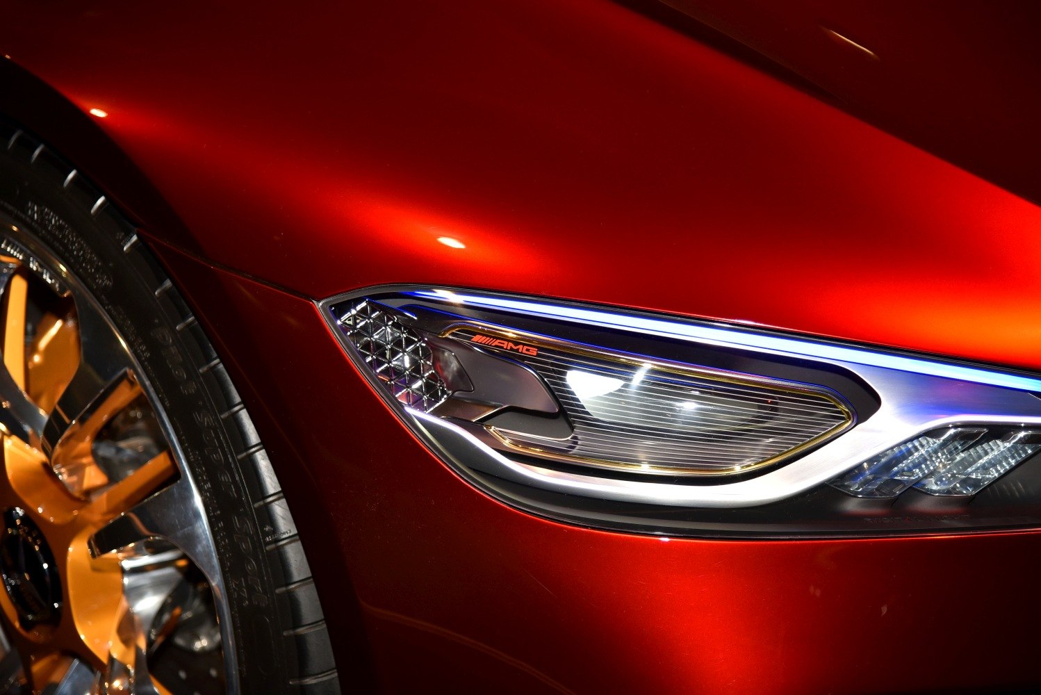 Close-up of angular front headlight and golden alloy wheel.