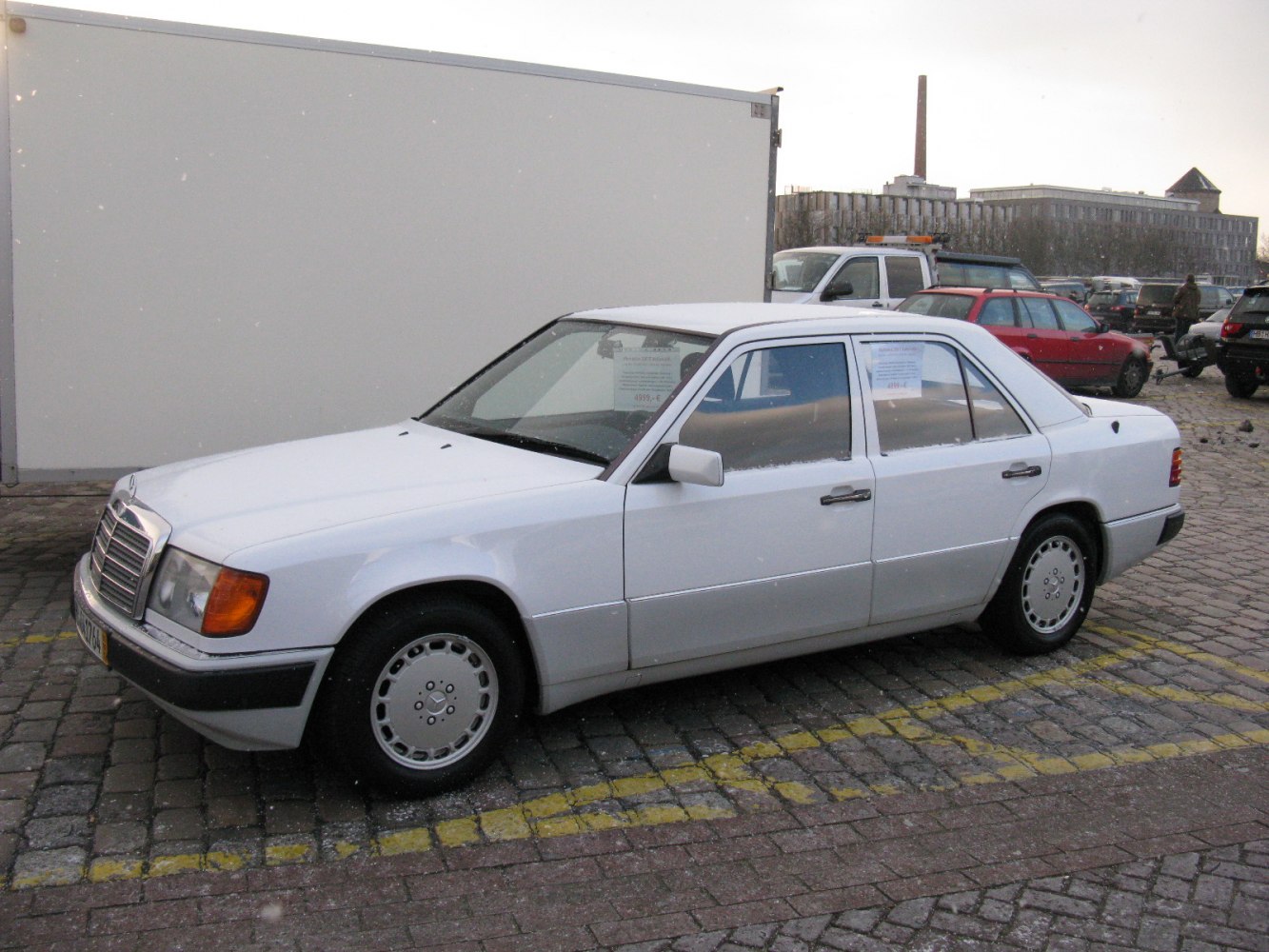 White four-door sedan on cobblestone with vintage rims and side mirrors