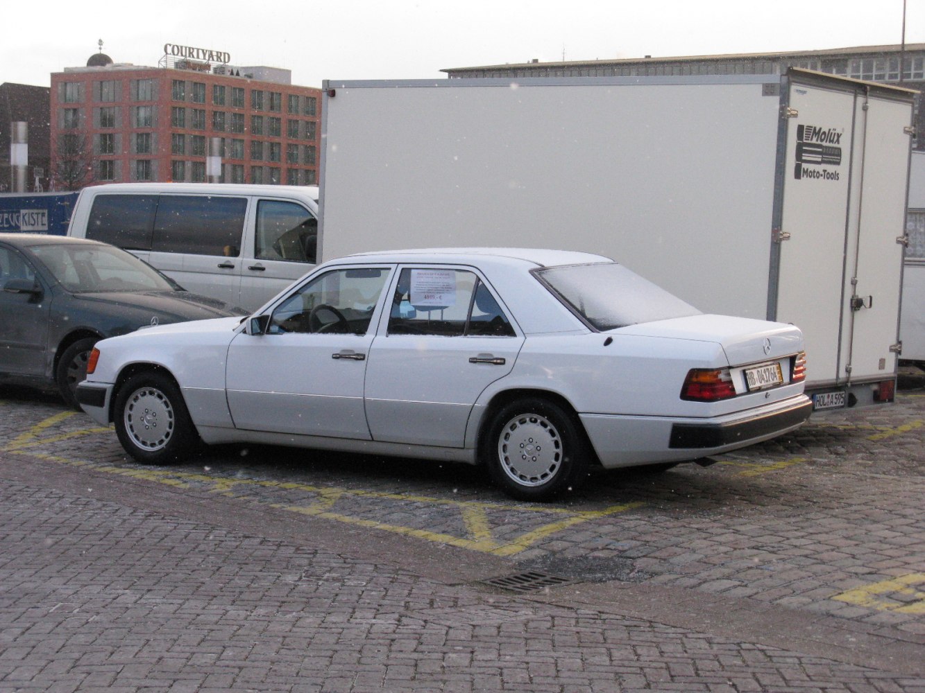 Side profile of a white 1989 sedan with alloy wheels parked on cobblestone.