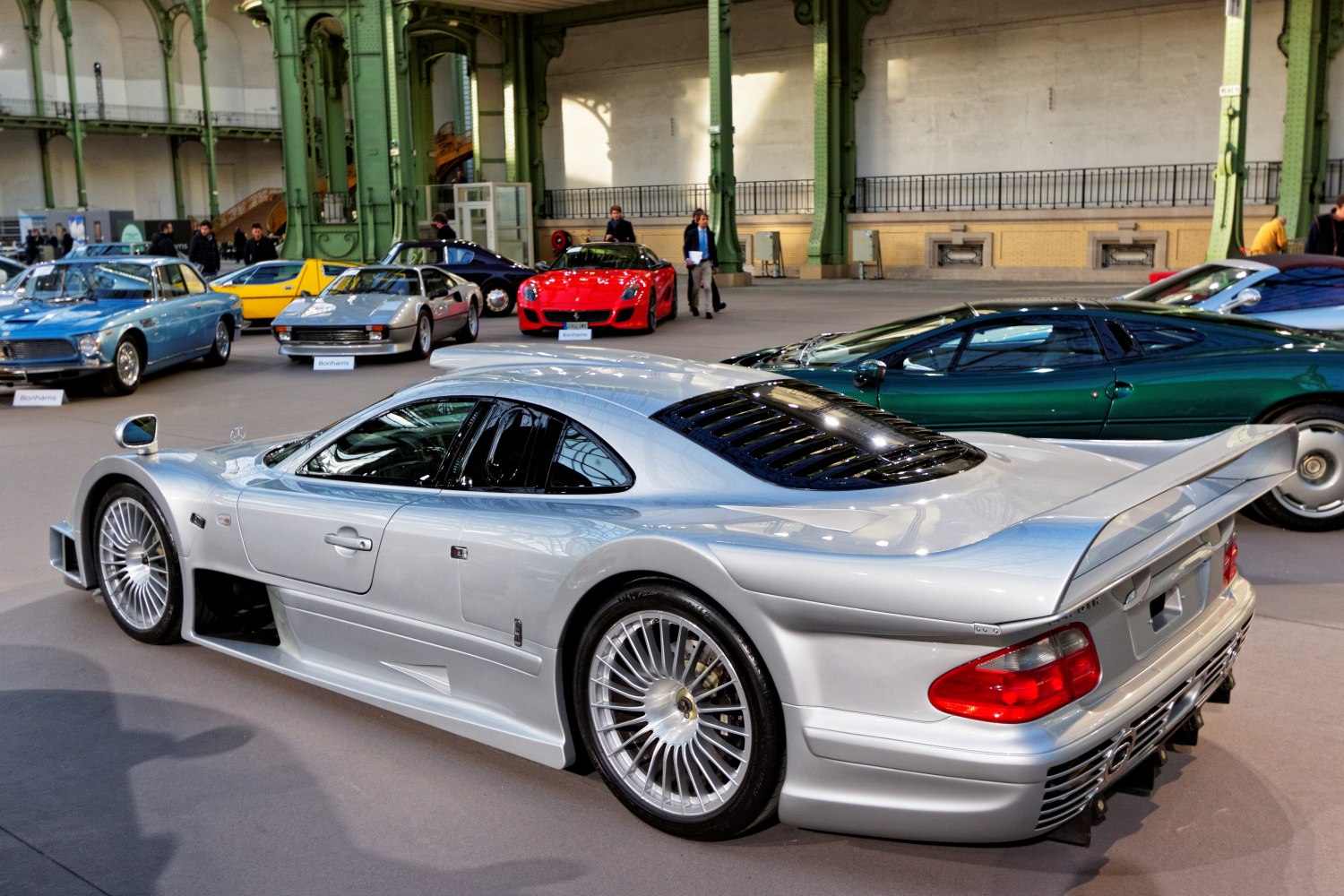Rear side view of silver mid-engine sports car with large rear wing and louvered window
