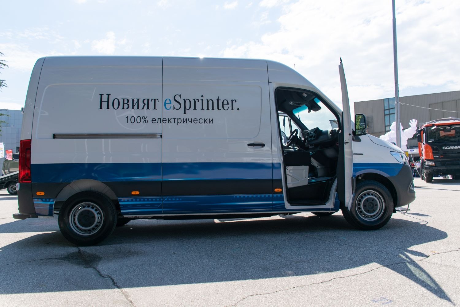 Side view of electric panel van with open driver door and blue-white body design