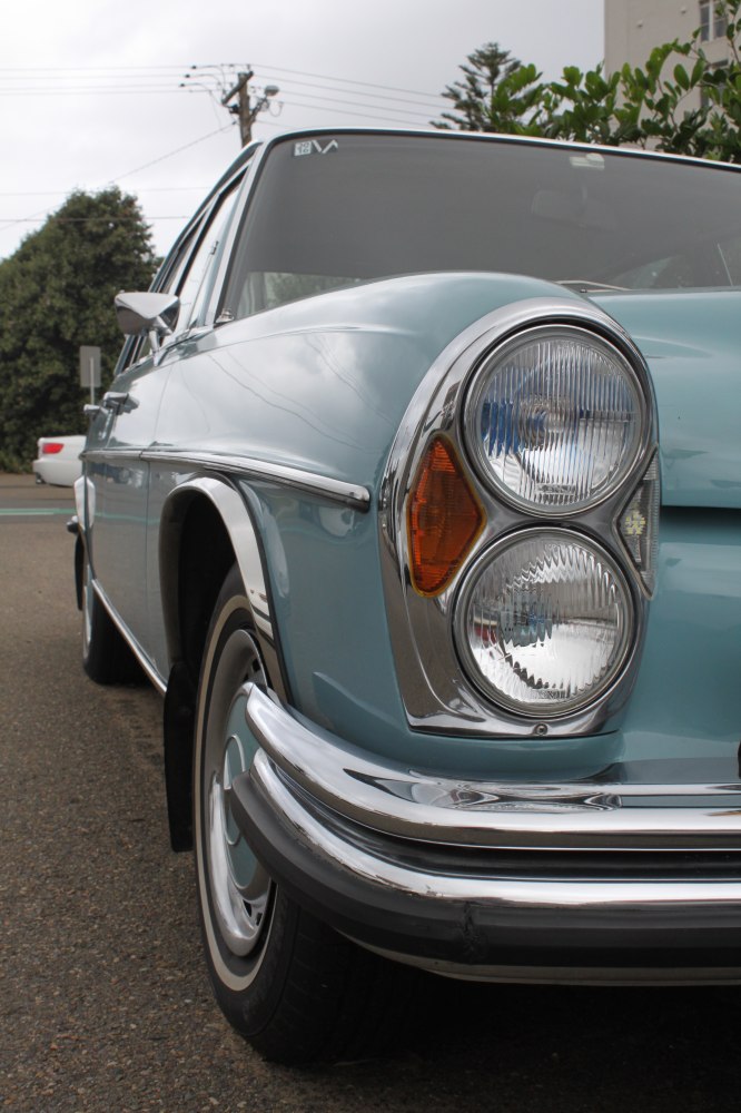 Dual round headlights and chrome bumper on vintage car front.