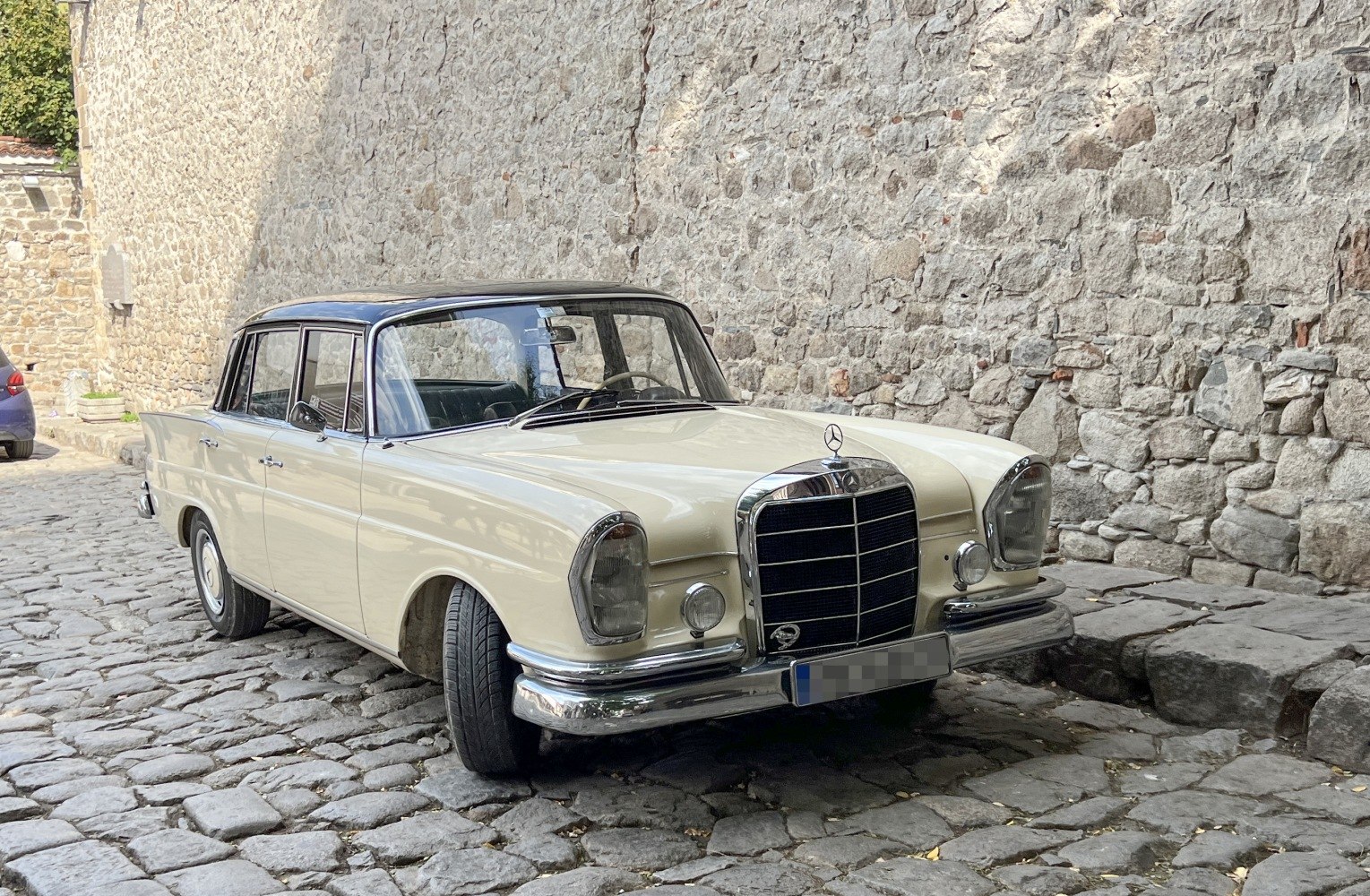 Beige vintage car with chrome grille and round headlights on cobblestone street