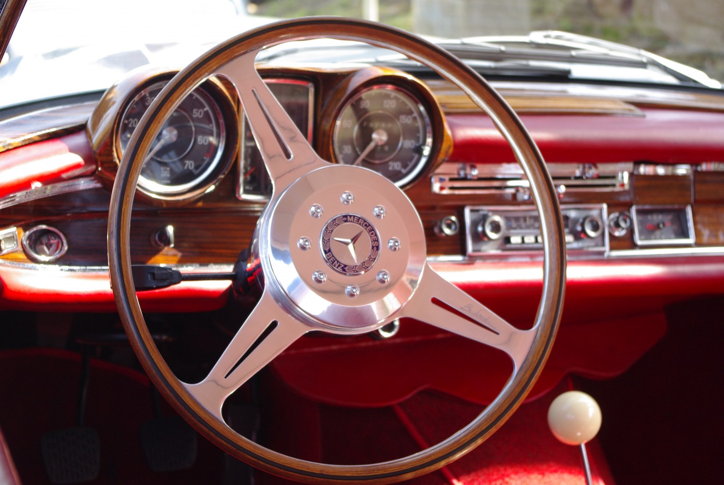 Wooden steering wheel and rich red dashboard with analog gauges and classic controls.