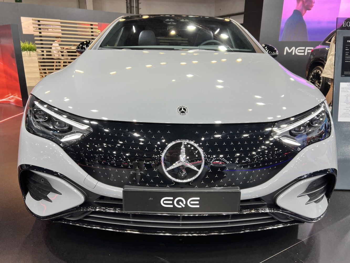 Glossy patterned grille and sleek LED headlights on electric sedan front.