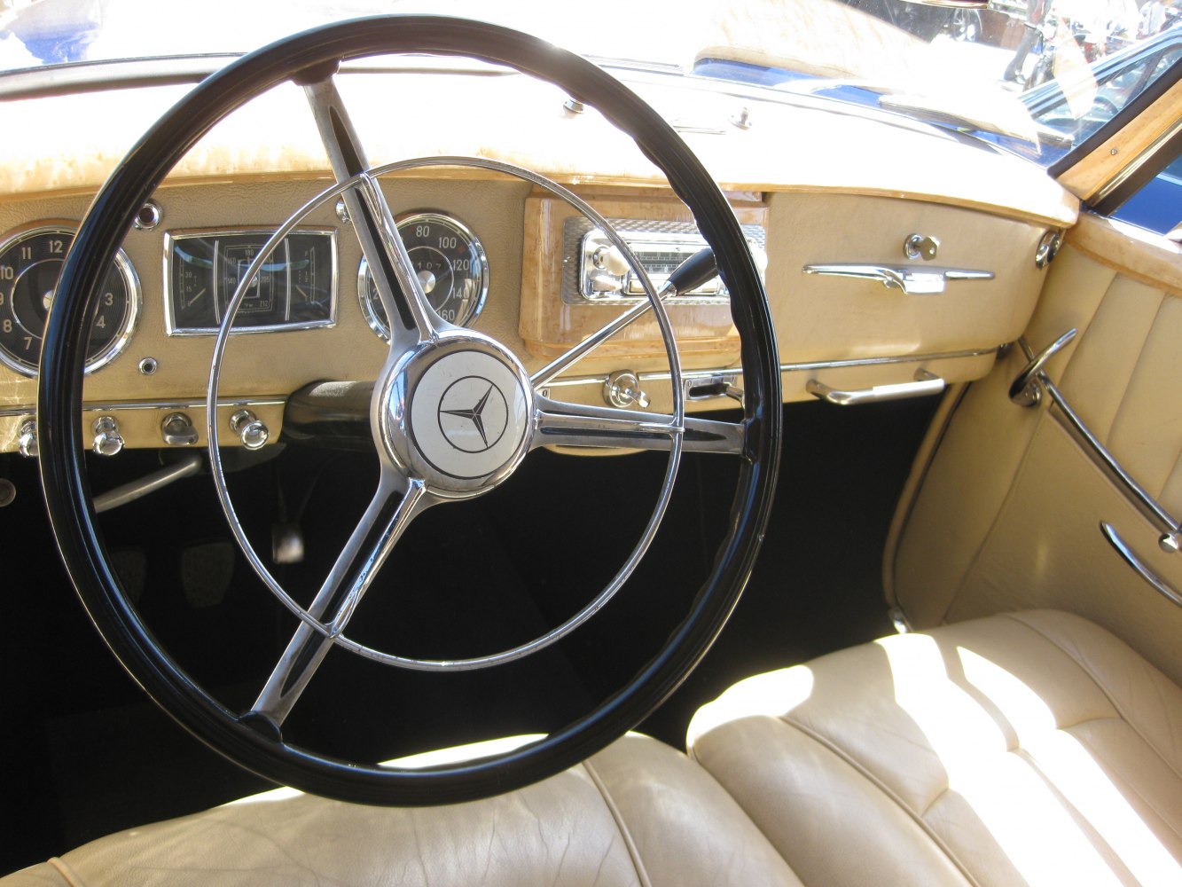 Classic vintage steering wheel and dashboard with analog gauges and beige leather upholstery.
