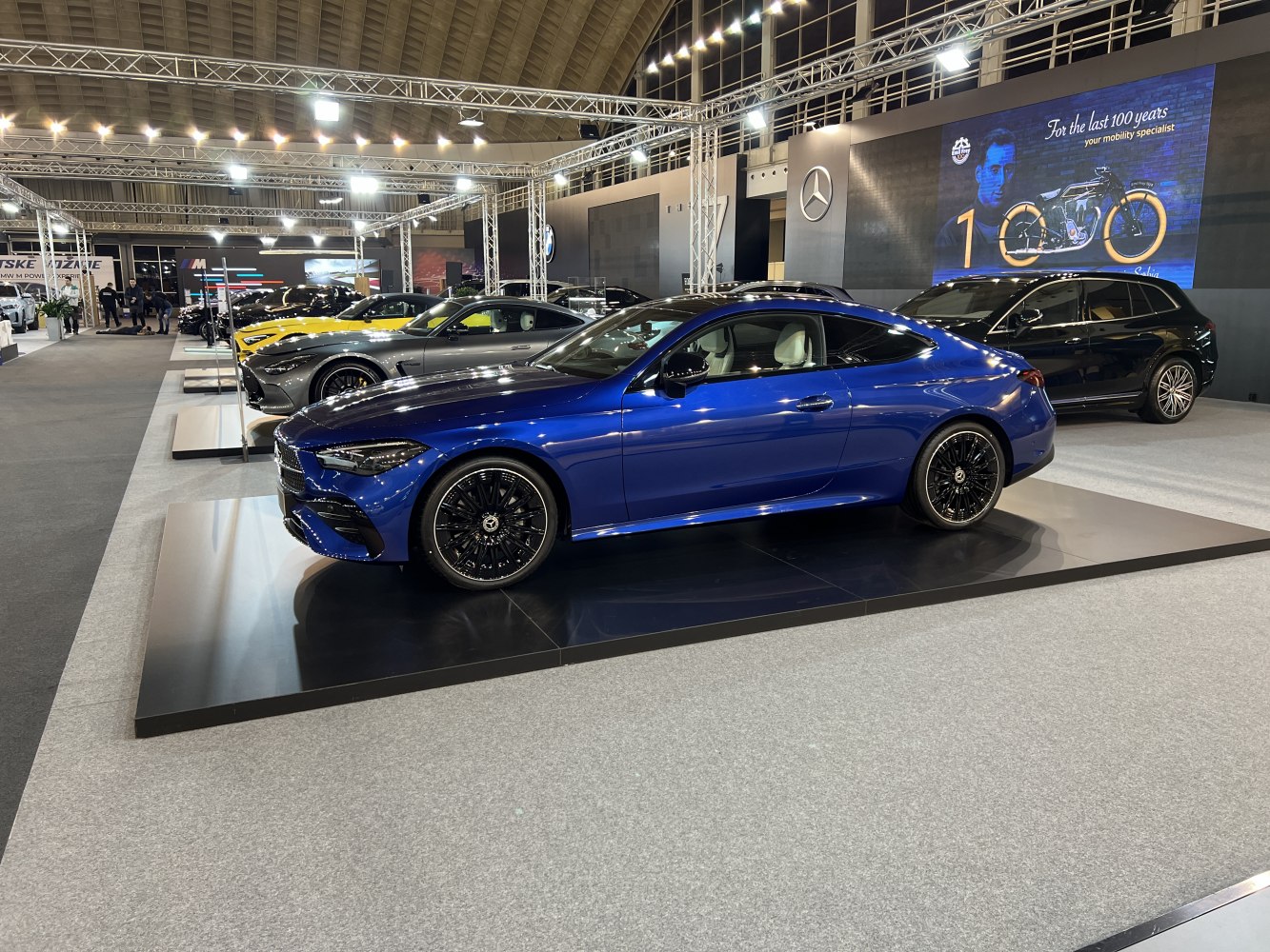 Luxury coupe in blue with black multi-spoke wheels on display indoors