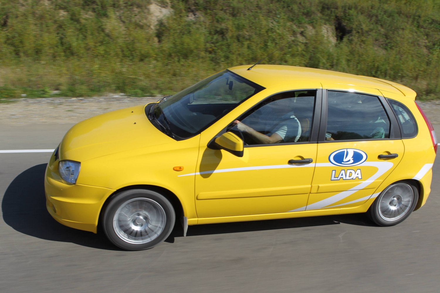 Yellow hatchback with sporty rims driving on road side view
