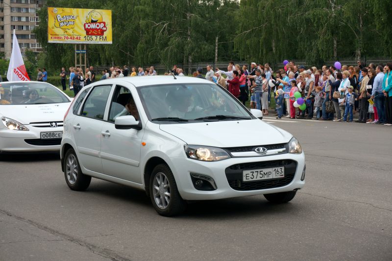White hatchback car front view driving on urban street with crowd