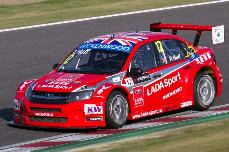 Red racing vehicle with aerodynamic modifications and large rear wing on racetrack