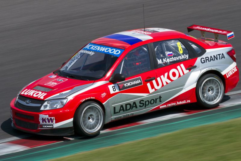 Red and white Lada Granta I Sport race car with Lukoil and racing decals on a track.