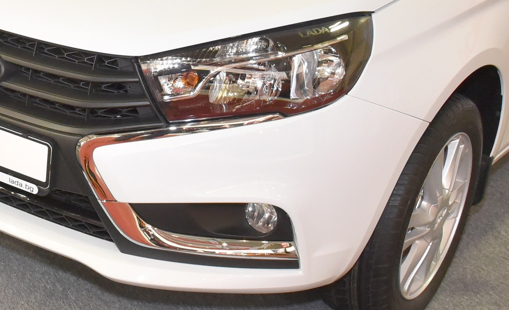 Front headlight, grille, chrome trim, and wheel detail of white car