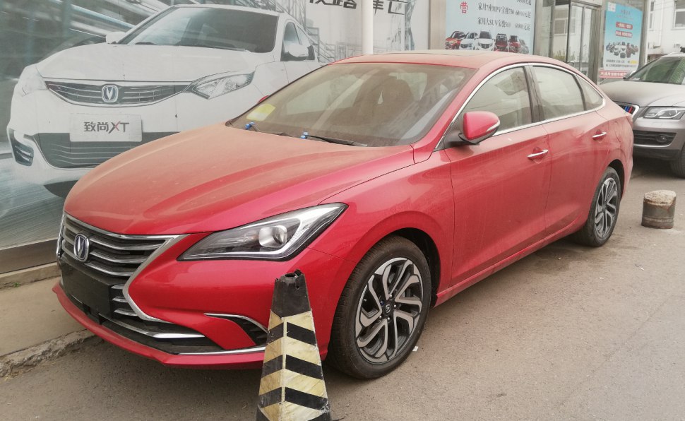 Red sedan with sharp LED headlights and alloy wheels in front side view