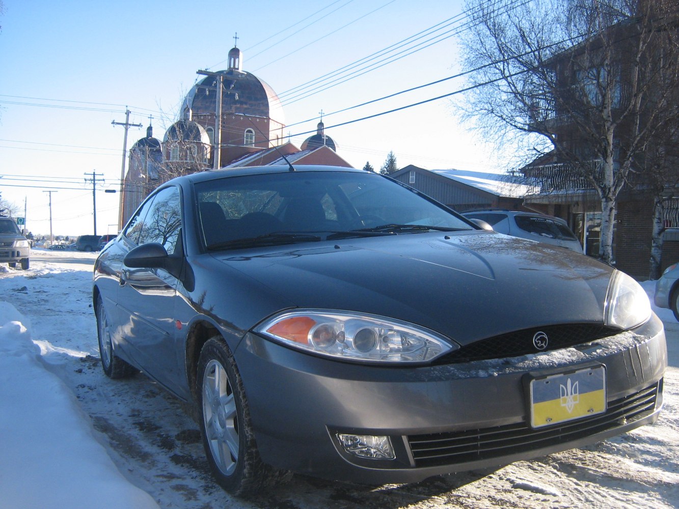 Front view of a car with distinctive headlights and hood on snowy street
