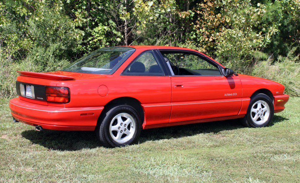 Red two-door coupe with rear spoiler and alloy wheels parked on grass