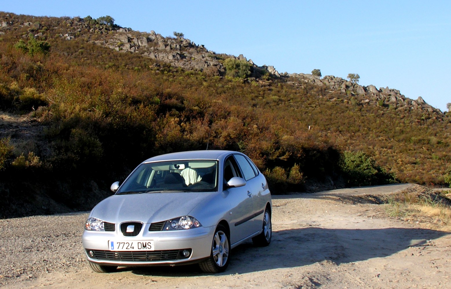 Silver hatchback front view with headlights and grille on gravel road