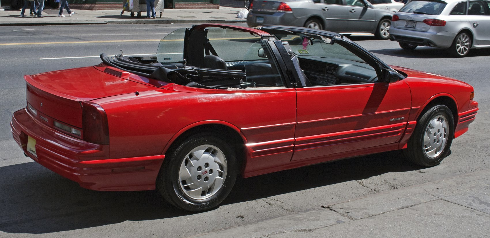 Red convertible with folded soft top and visible interior from passenger side