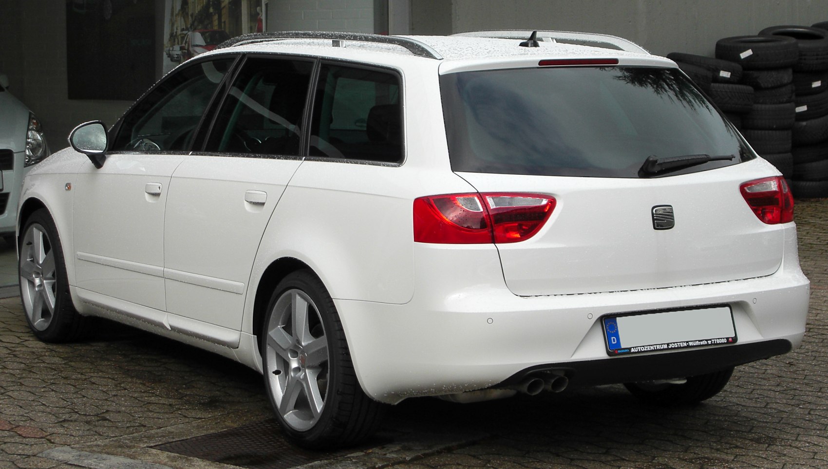 Rear side view with dual exhaust and roof rails of a white estate vehicle