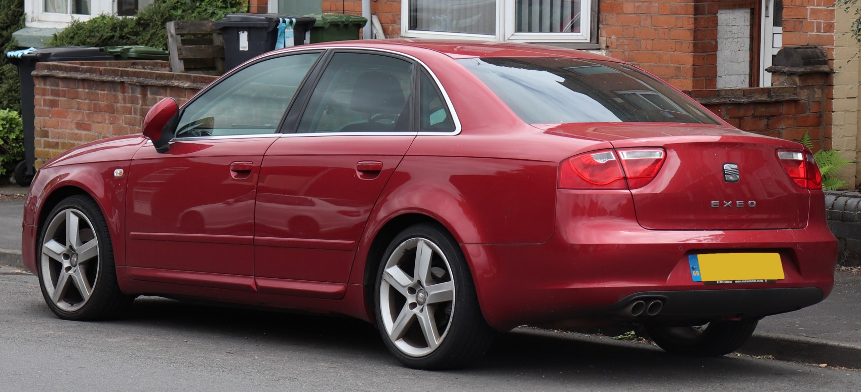 Red sedan rear side with alloy wheels and dual exhaust