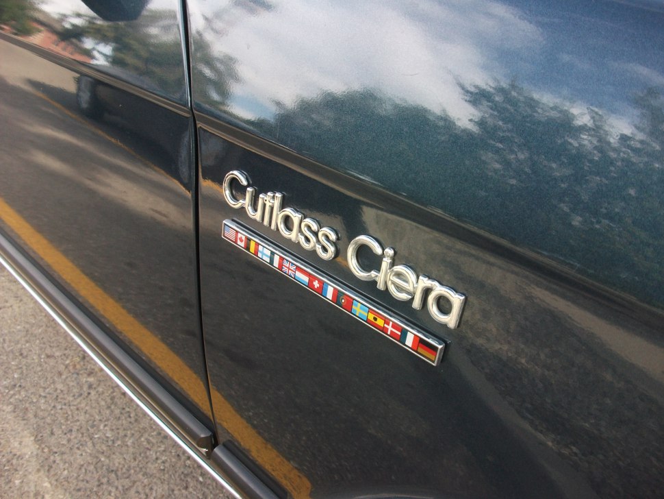 Close-up of Cutlass Ciera badge with international flags
