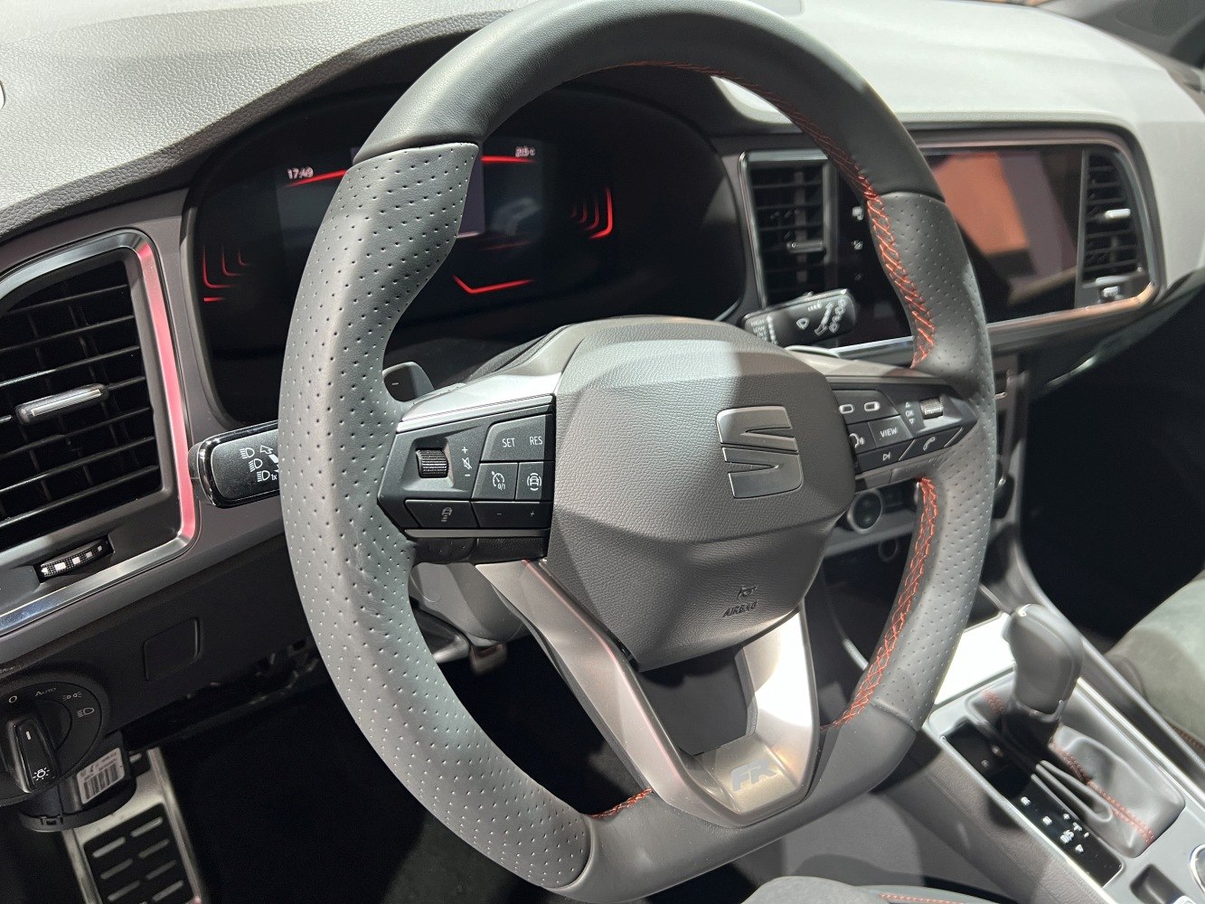 Steering wheel with perforated leather grips and red stitching, featuring multi-function buttons.