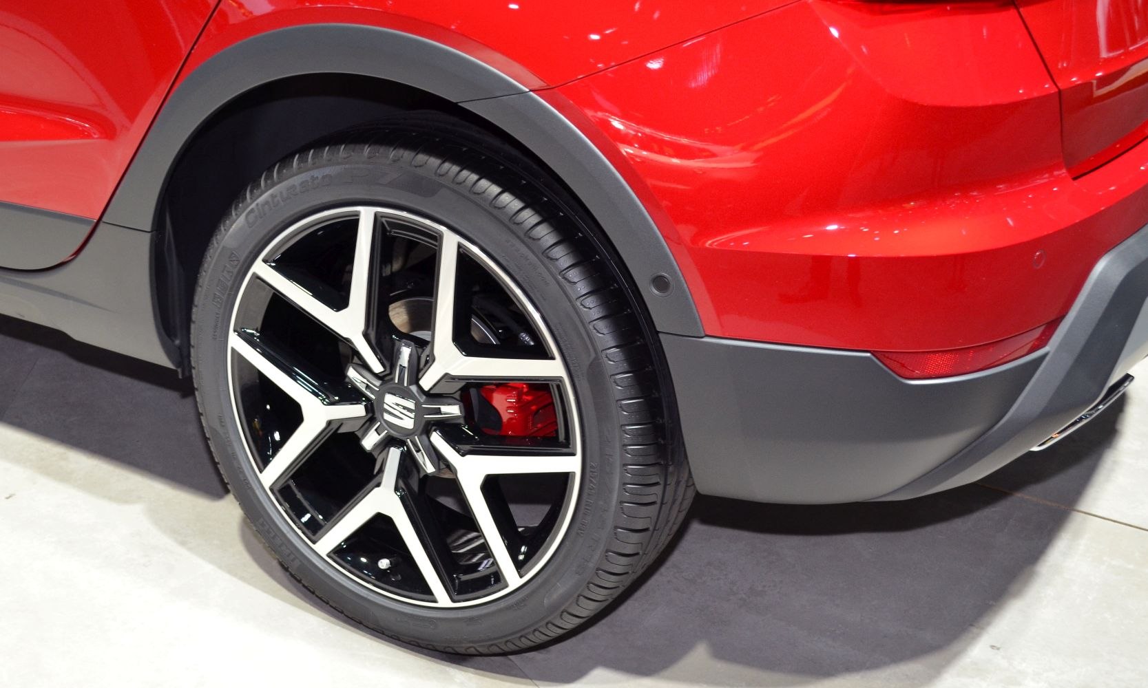 Close-up of black and silver alloy wheel with red brake caliper and rear quarter panel.