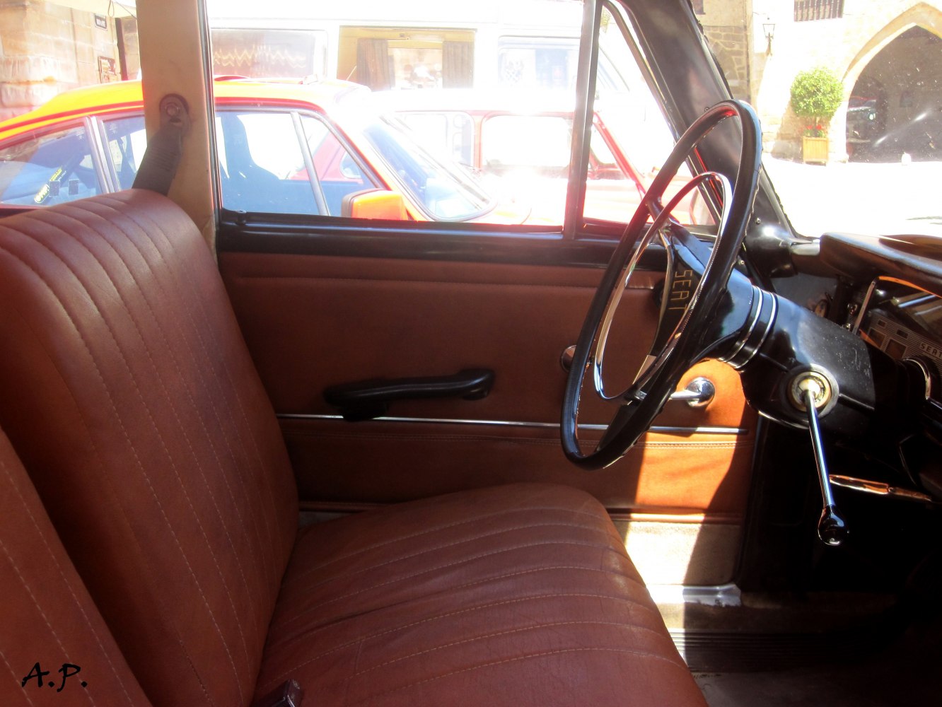 Vintage brown car interior with right-hand steering wheel and manual window crank