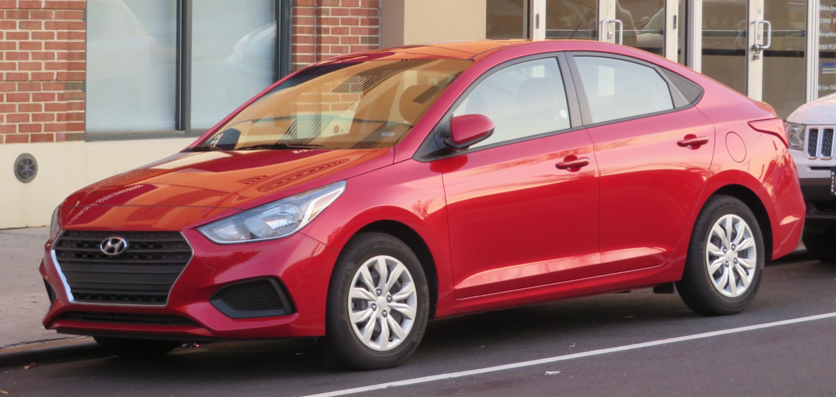 Front-side profile of red compact sedan with angular headlights and multi-spoke wheels