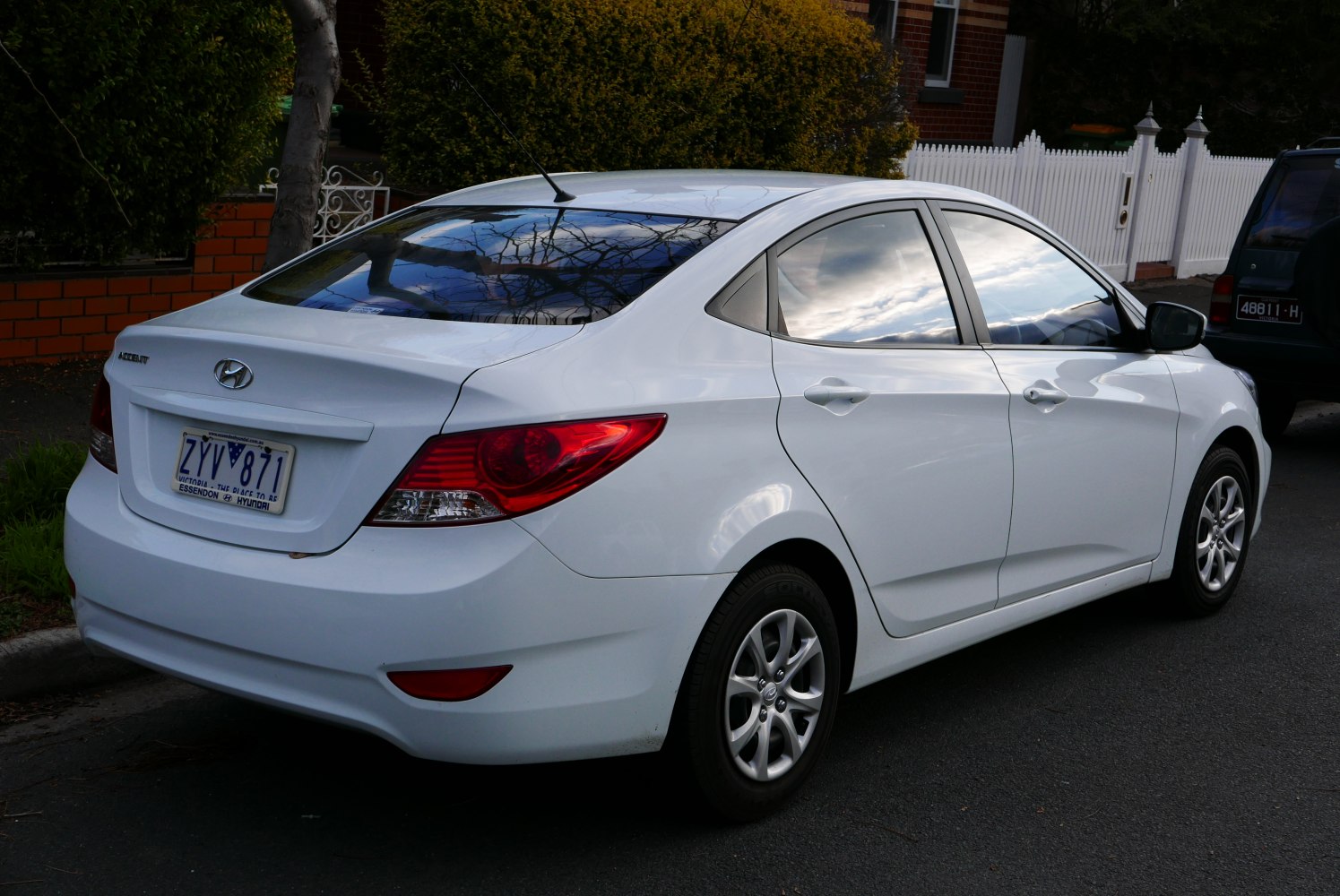 Rear side view of white four-door sedan with red taillights and alloy wheels