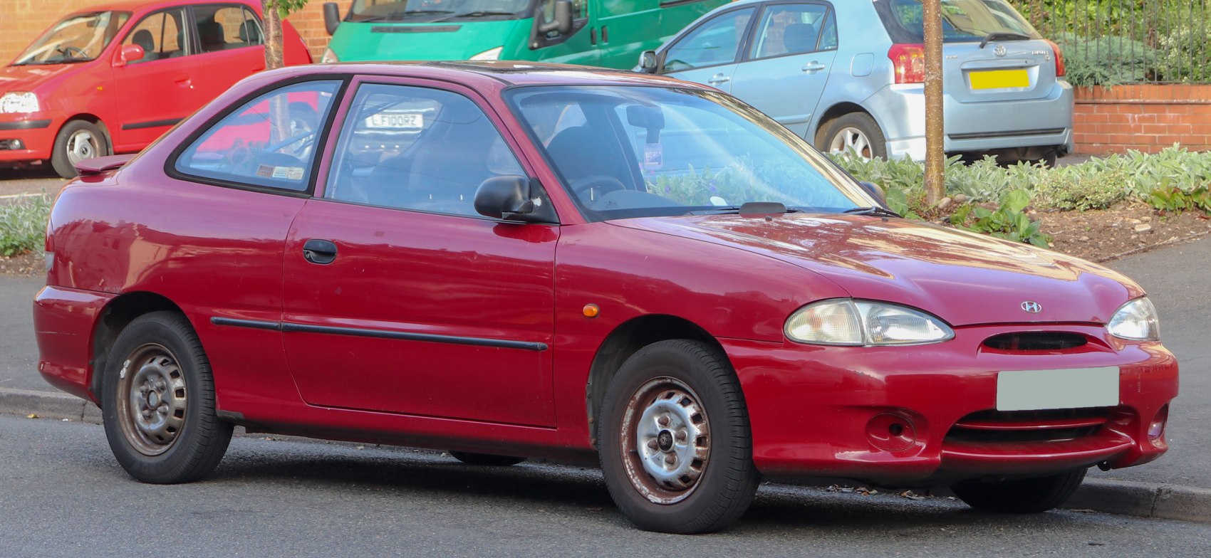 Red compact hatchback, rounded headlights, small rear spoiler, black side moldings