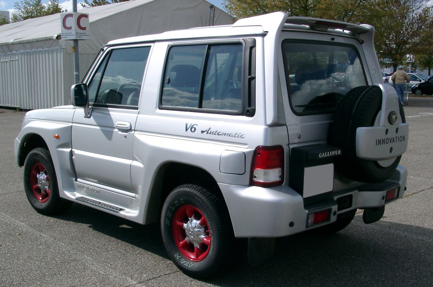 Silver SUV with V6 badge, red rims, and rear-mounted spare tire