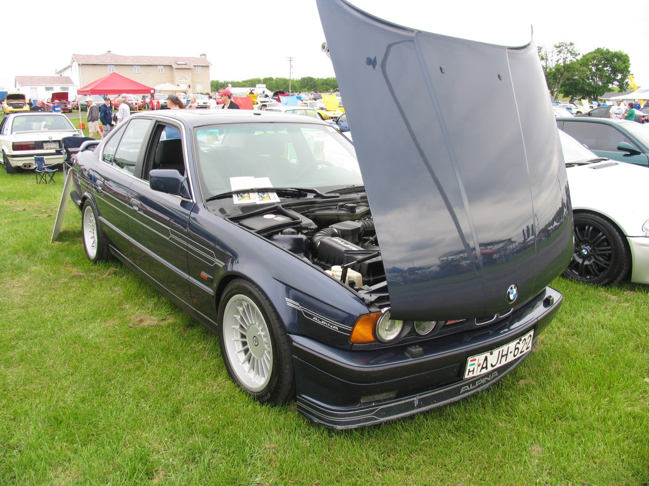 Classic dark blue sedan with open hood revealing engine at outdoor car show