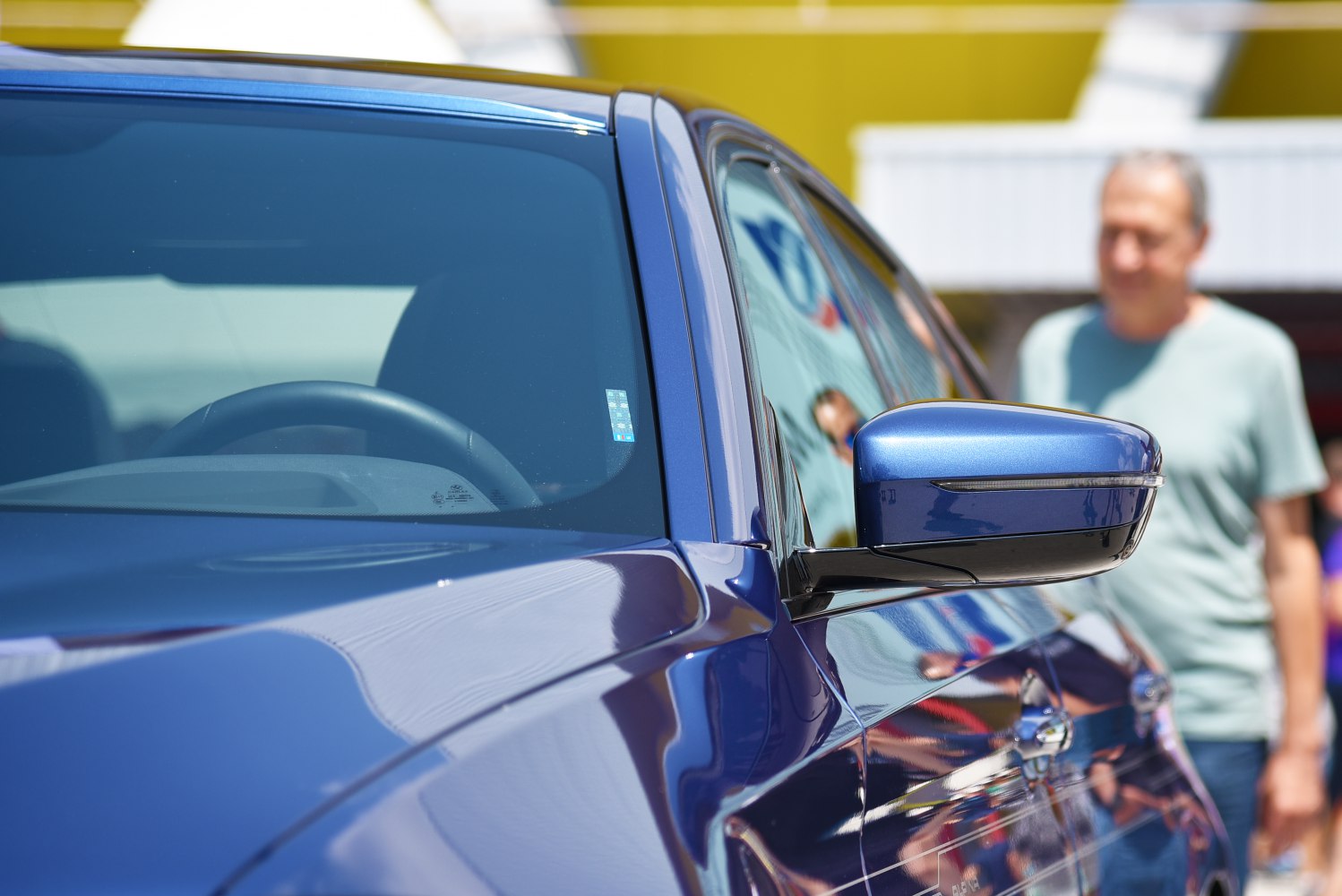 Close-up of a car side mirror and window with reflective blue paint.
