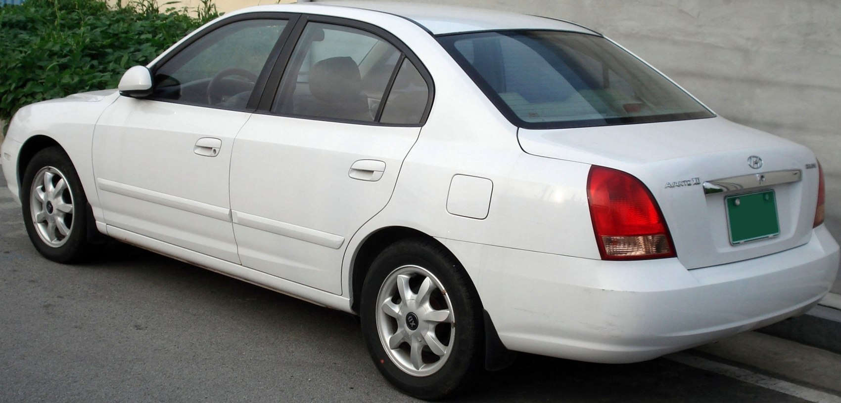 White compact sedan rear side with distinct tail lights and alloy wheels