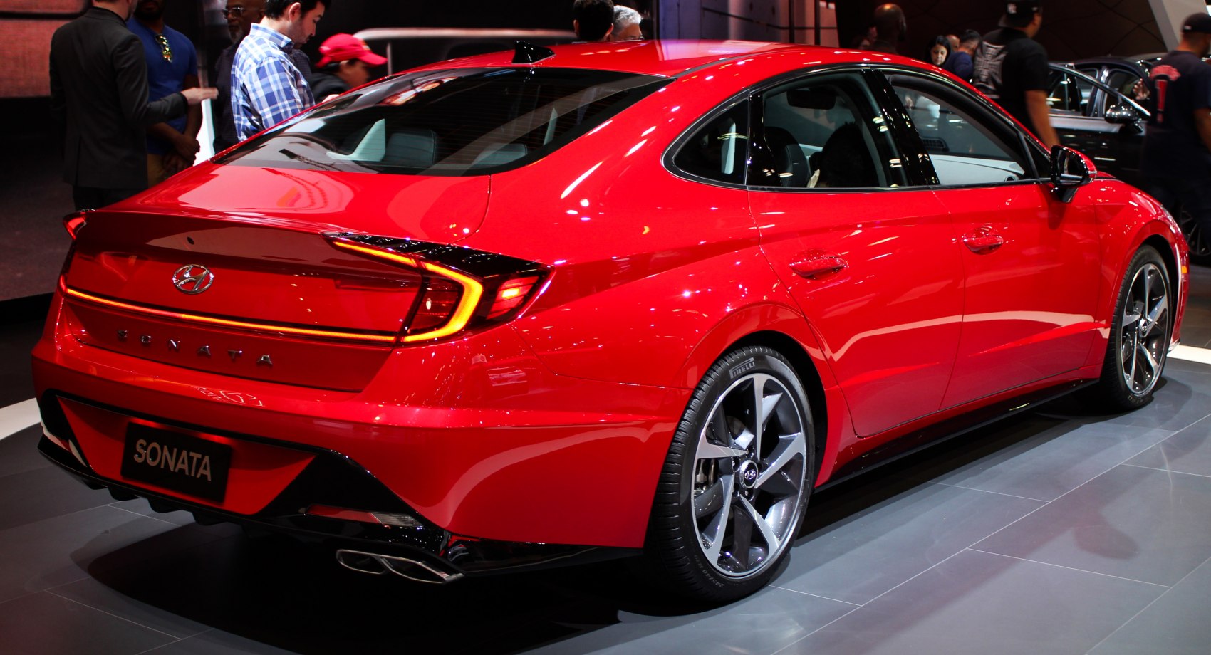 Rear view of a red modern sedan with LED tail light strip and sporty wheels
