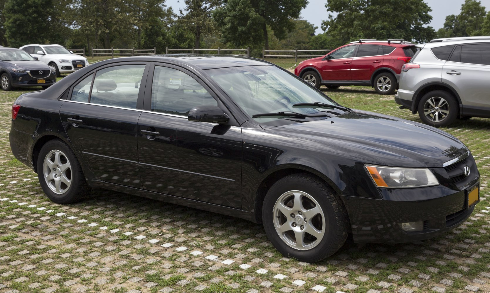 Side profile of a black sedan with alloy wheels parked outdoors.