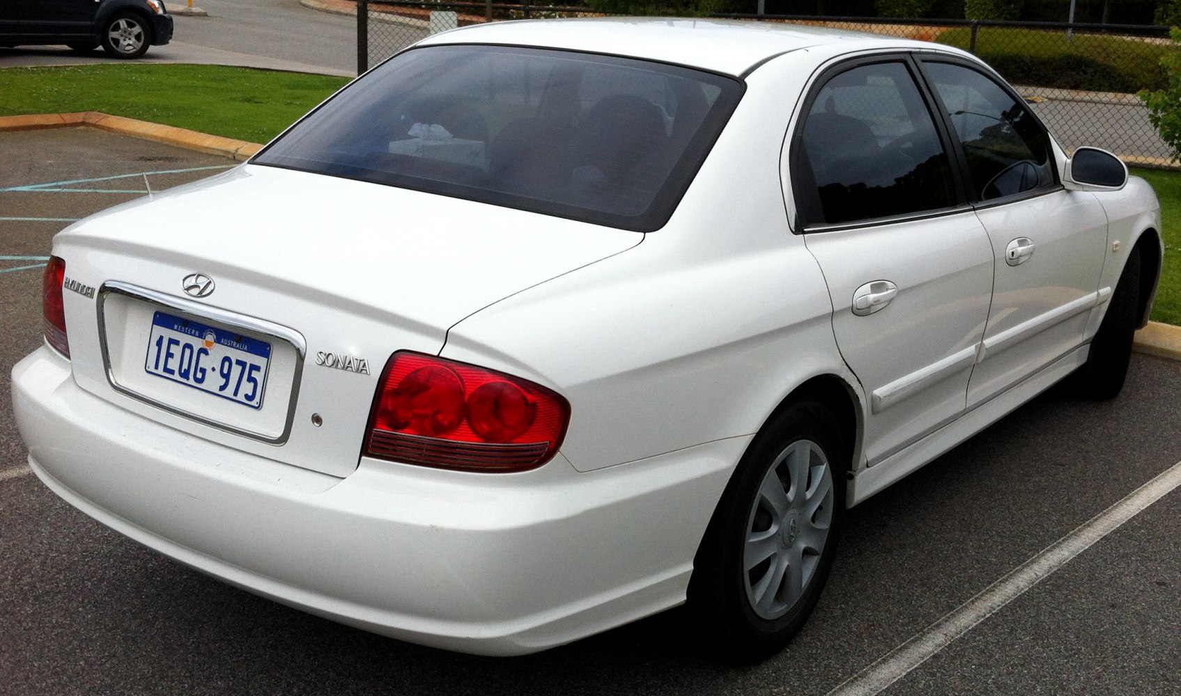 Rear and side view of a white four-door sedan with red taillights.