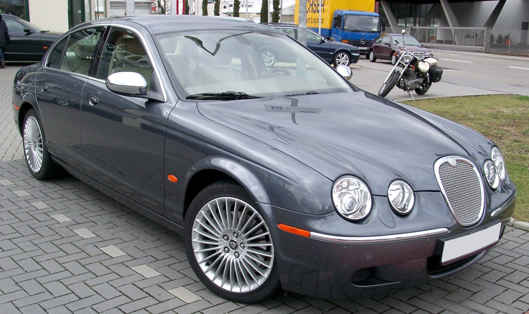 Front side view of a luxury sedan with quad round headlights and multi-spoke alloy wheels