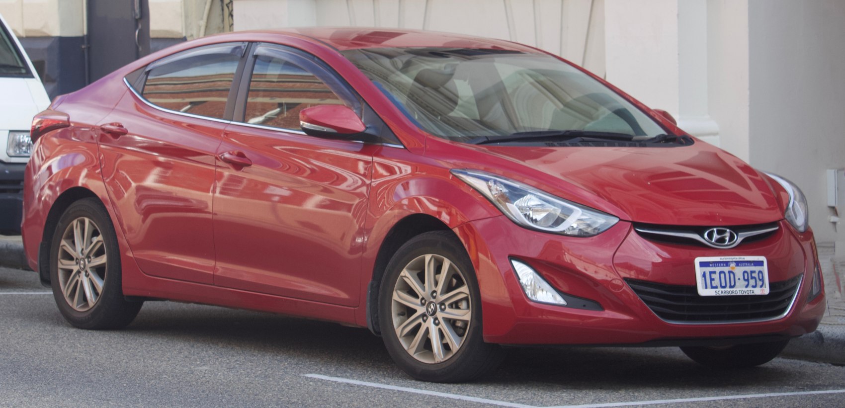 Red sedan with sleek headlights and alloy wheels, front side view.
